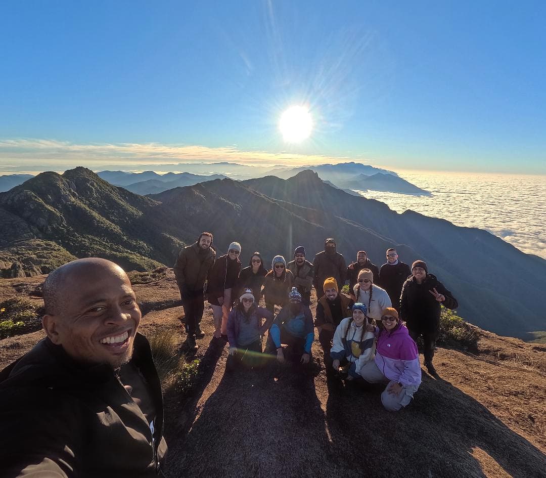 Selfie do guia com a turma no cume, com o sol e o mar de nuvens ao fundo