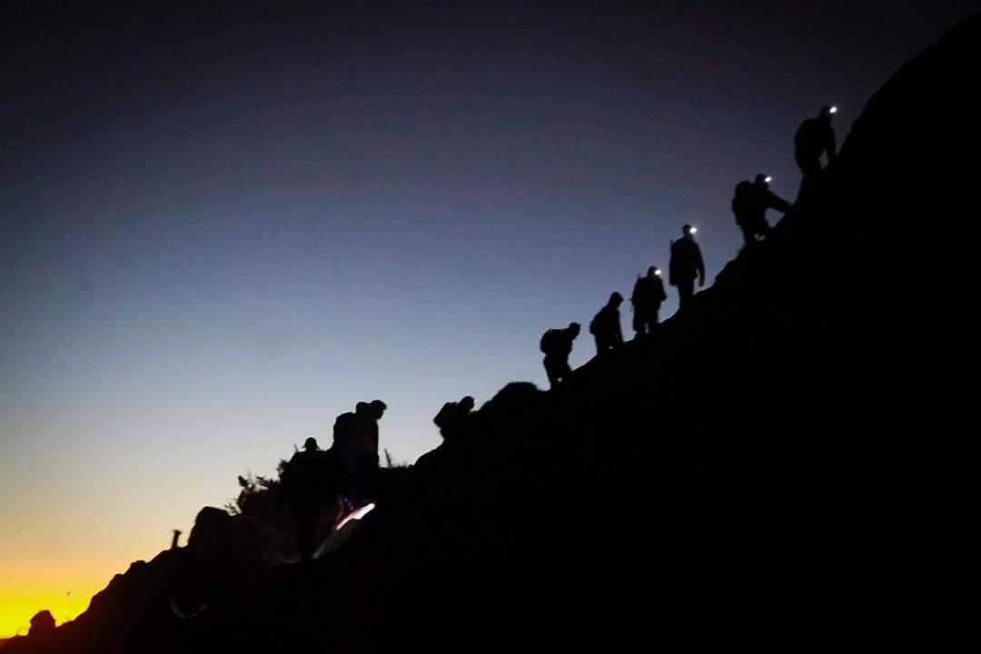 Grupo subindo a montanha no escuro, de lanterna de cabeça, com o céu clareando